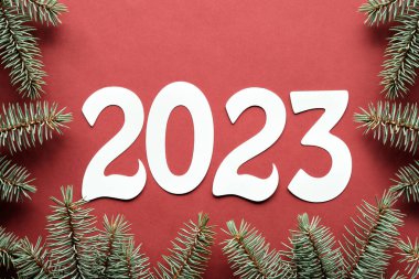Kırmızı arka planda 2023 kağıt numarasının taslağı. Düz, kırmızı arka plan, doğal köknar dalları. Mutlu Noeller, mutlu yıllar. Kış tatili için doğal dekoru olan tebrik kartı tasarımı.
