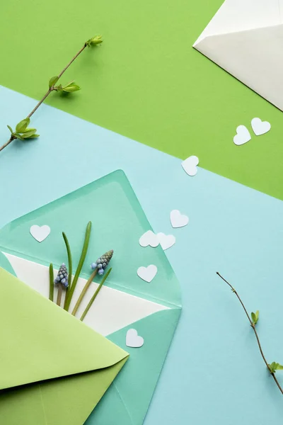 緑の色合いの春の背景 グリーティングカードと黄色のエランシスの花と紙の封筒 層状の単色幾何学的な紙の背景にハートコンフェッティ — ストック写真