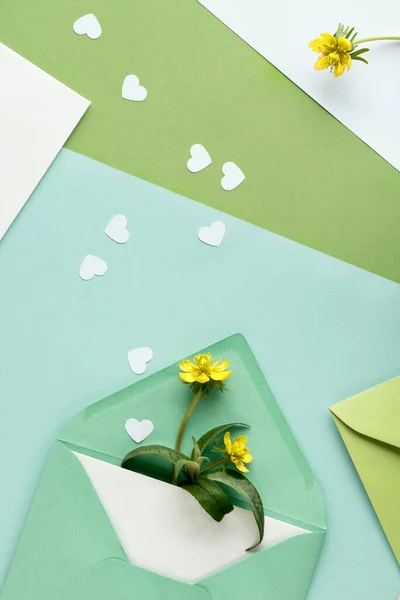 春天的背景是绿色的 有贺卡和黄色差事的纸制信封这朵花 色彩斑斓的多层单色几何纸制背景上的心形花纹 — 图库照片