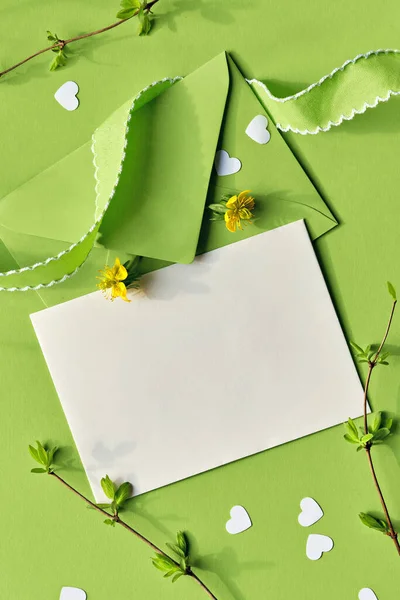 緑の色合いの春の背景 グリーティングカードと黄色のエランシスの花と紙の封筒 緑と白の紙の背景にハートのコンフェッティ — ストック写真