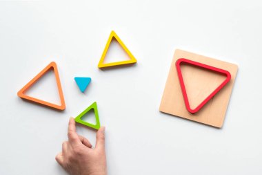 Gökkuşağı renginde yuva yapmış ahşap üçgenler. Ortak merkezli eğitim figürleri. Bebek istifleme bulmacası. Montessori bebek ve çocuklar için duyusal bir hediye. Düz konum, beyaz kağıt arkaplanda üst görünüm.