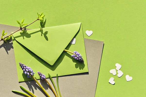 緑の色合いの春の背景 青ブドウのヒヤシンスの花と紙の封筒 緑と銀の紙の背景にハートコンフェッティ 葉のついた新鮮な小枝 フラットレイアウト トップビューの春の配置 — ストック写真