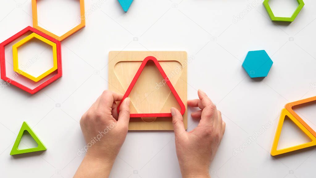 Hands with triangle. Nested wood triangles and hexagons, concentric figures. Stacking puzzle, Montessori nesting sensory gift for toddlers and kids. Flat lay, top view on white paper background.