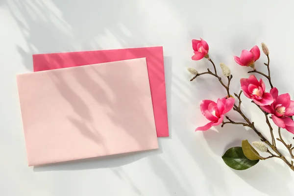 封筒付きの空白のポストカード ピンクの装飾的なマグノリアの花 白い背景の上からの眺め 自然の直射日光 長い影 — ストック写真