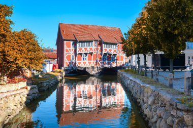 Gewolbe, old red timbered house in Wismar. Mecklenburg-Vorpommern, Germany with reflection in river Grube on bright Autumn day with blue sky.