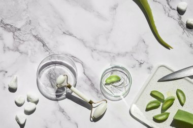 Aloe vera home made moisturizer and white stone face roller on off white marble background. Beauty treatment background, lat lay, top view. Facial massage concept, handmade cosmetics.