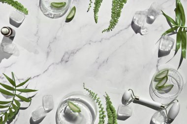 Self made aloe moisturizer and green jade face roller. Exotic fern leaves on off white marble background. Minimal flat lay, top view. Facial massage concept, handmade cosmetics.