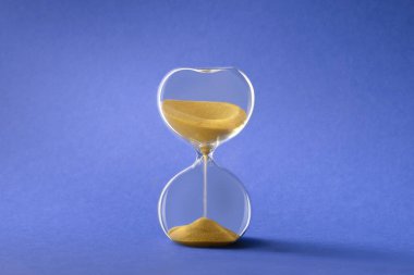 Hourglass, also known as sandglass or sand timer. Single glass sand clock with golden sand on blue paper background. Design element,