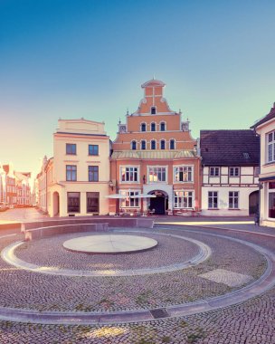 Old historic buildings in Wismar, Germany. Empty circular square early morning. Sunny day with blue sky, sun flare.