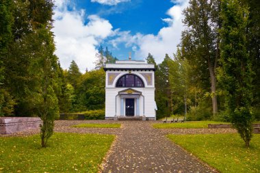 Mausoleum of war general Michael Andreas Barclay de Tolly. Small white chapel in the end of long oak alleyway. Blue sky with clouds, sunny day in Jogeveste Estonia.