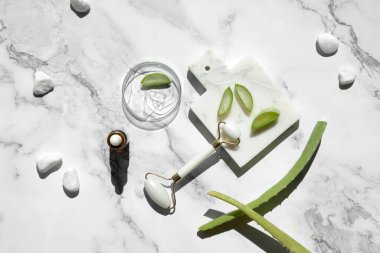 Aloe vera home made moisturizer and white stone face roller on off white marble background. Beauty treatment background, lat lay, top view. Facial massage concept, handmade cosmetics.