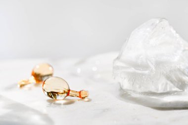 Serum capsules in petri dish for healthy skin with ice balls. Anti-wrinkle rejuvenation skin treatment. Beauty product presentation. Off white stone marble background.