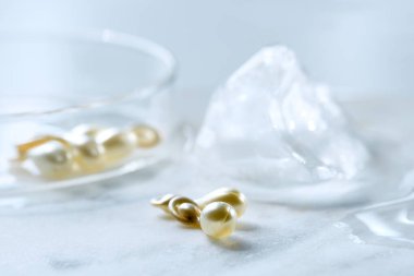 Serum capsules in petri dish for healthy skin with ice balls. Anti-wrinkle rejuvenation skin treatment. Beauty product presentation. Off white stone marble background.