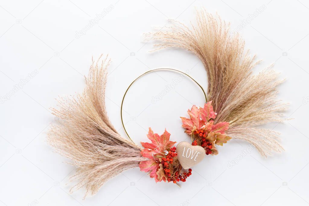 Dried floral wreath from dry pampas grass and Autumn maple leaves on metal frame. Flat lay on white table, soft natural sunlight.