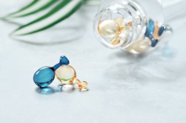 Serum capsules for healthy skin. Anti-wrinkle rejuvenation skin treatment. Beauty product presentation with green monstera leaves. Close-up in blue and orange capsules.