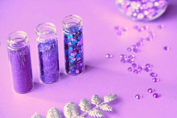 All kinds of glitter products on pink sparkling background. Close-up on vials, bottles with various glitter makeup in neon pink, blue and turquoise shades. Scattered strasses, rhinestones.