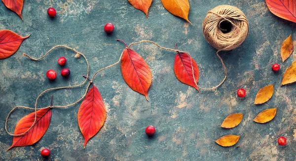 Panoramic banner image with natural garland, red cherry leaves tied on hemp cord. Natural Fall decorations, panorama of vibrant red and orange leaves. Flat lay on dark background.