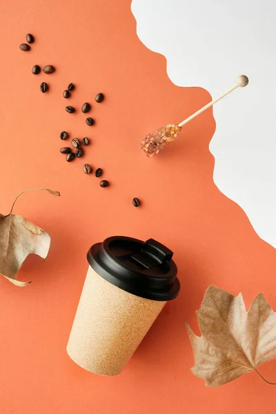 Coffee mug with natural cork band. Coffee cup to go on orange white Autumn background with dry sycamore leaves. Coffee beans and sugar stick. Vertical creative background for social media stories.