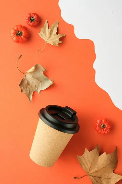 Coffee mug with natural cork band. Coffee cup to go on orange white Autumn background with dry sycamore leaves and deco pumpkins. Flat lay, top view. Vertical background for social media stories.