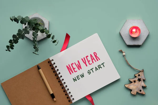 Text New Year, new start in notebook, journal. Mint green background, flat lay with eucalyptus twigs, Xmas tree wooden trinket, candle on marble hexagon. New Year motivation message, motivator.