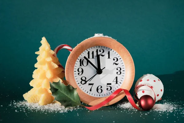 Countdown to midnight. Wood alarm clock with new year 2023. White baubles with polka dots and beeswax Christmas tree. Green paper background with snow.