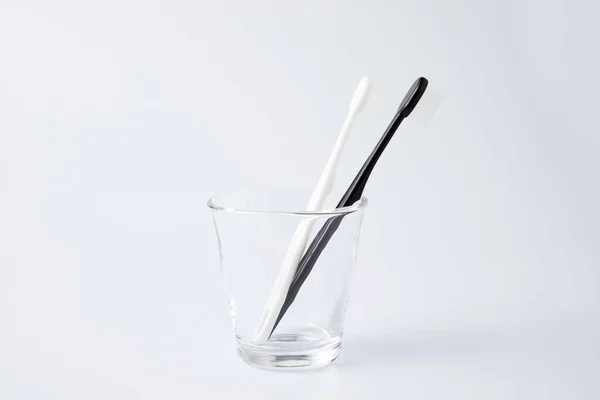 Cepillos de dientes negros blancos en artículos de tocador de vidrio aislados sobre fondo blanco — Foto de Stock