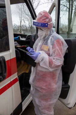 Ambulansın yanında anti-virüs kıyafeti giymiş bir sağlık görevlisi kız tableti dolduruyor..