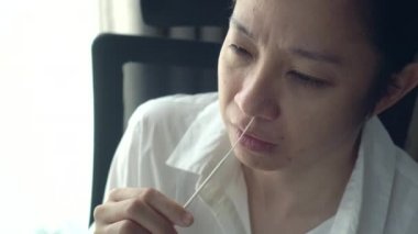 Asyalı kadın antijen test kiti yapıyor. ATK derin burun değiştirme gözyaşı. Rahatsız edici bir duygu içinde ağlıyor.