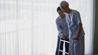 Yaşlı çift rehabilitasyon terapisi yapıyor. Walker 'la hastane afişlerinde yürüme pratiği yapıyorlar.