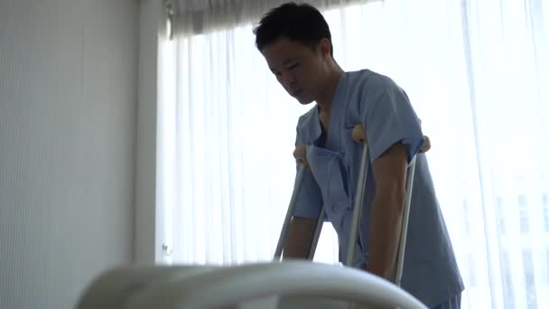アジア系成人男性が病院の部屋で医療費を心配しながら松葉杖で歩く負傷 — ストック動画