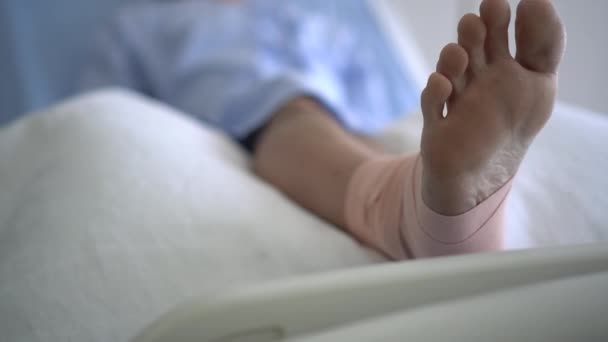アジアの男はベッドの回復に横たわって事故から彼の足を傷つけた傷と疲れ — ストック動画