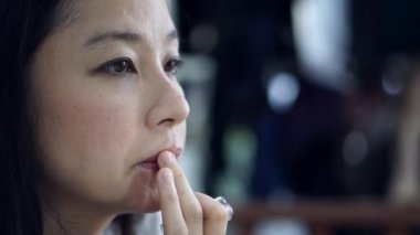 Asyalı orta yaşlı kadın makyaj yapıyor. Kırmızı ruj sürüyor. Ağır çekimde.