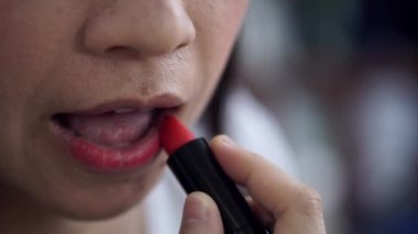Dudaklarına kırmızı ruj süren Asyalı kadın makyaj yapıyor.