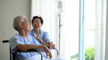 Yaşlı Asyalı yaşlı çift tekerlekli sandalyede sohbet ederken konuşuyor.