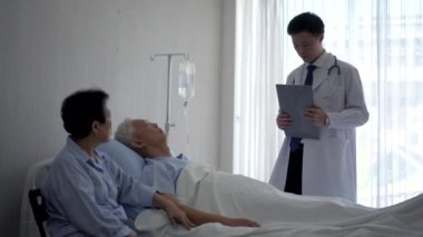 Asyalı genç doktor tedavi odasında yaşlı yaşlı bir hastaya tavsiye veriyor.