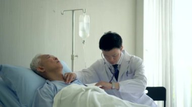 Hastanedeyken yaşlı hasta nabzını kontrol eden Asyalı bir doktor.
