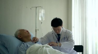 Hastanedeyken yaşlı hasta nabzını kontrol eden Asyalı bir doktor.