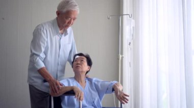 Asyalı yaşlı koca yaralı karısını tekerlekli sandalyeden alıp hastane penceresinden manzarayı izlemeye götürdü.