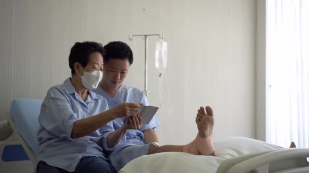 電話でソーシャルメディアについての会話を共有する病院のベッドで足を誘導したアジアの母親と息子 — ストック動画