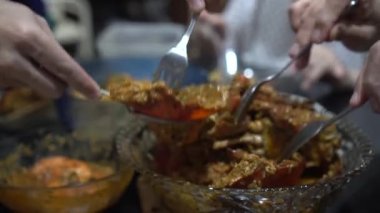 Çin ailesi, büyük kase yemeğinden Singapur biberli yengeç baharatlı baharat sosu yiyorlar.