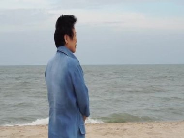 Havalı stil sahibi Asyalı son sınıf öğrencisi. Plaj kot ceketi giysisinde mutlu gülümsüyor.