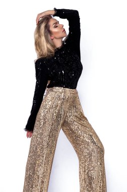 Kış zarif moda. Stüdyoda beyaz arka planda izole edilmiş kışlık pullu güzel ve zarif bir kadın. Model şık bir kazak ve modaya uygun pullu pantolon giyiyor. Vogue.