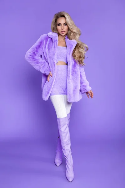 冬のファッション スタジオで紫色の背景にライラック毛皮の美しい幸せなブロンドの女性 モデルはスタイリッシュなバイオレットファーコート パープルセーター ライラックブーツを着用しています ヴォーグ カラフルなファッション — ストック写真