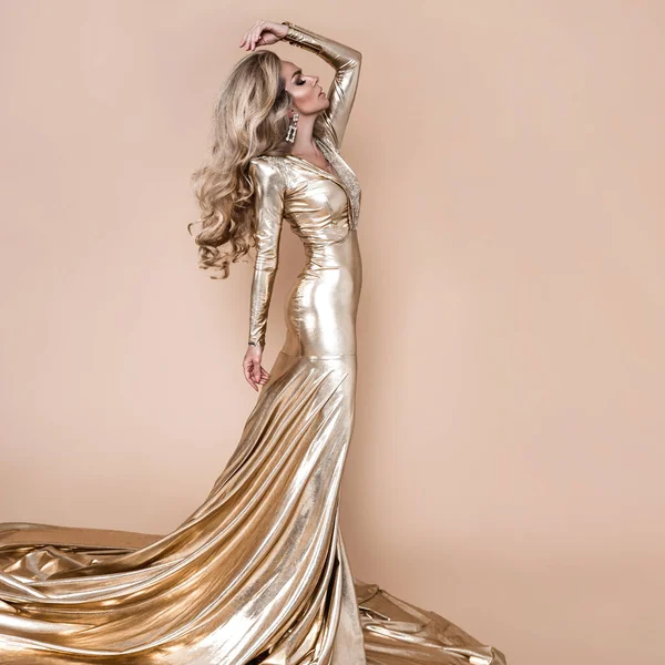 エレガントなファッション エレガントな長い金のドレスとベージュの背景に完璧な髪型で見事なブロンドの女性 豪華な夜のファッション グラマーファッションモデル 優雅さ 黄金のドレス — ストック写真