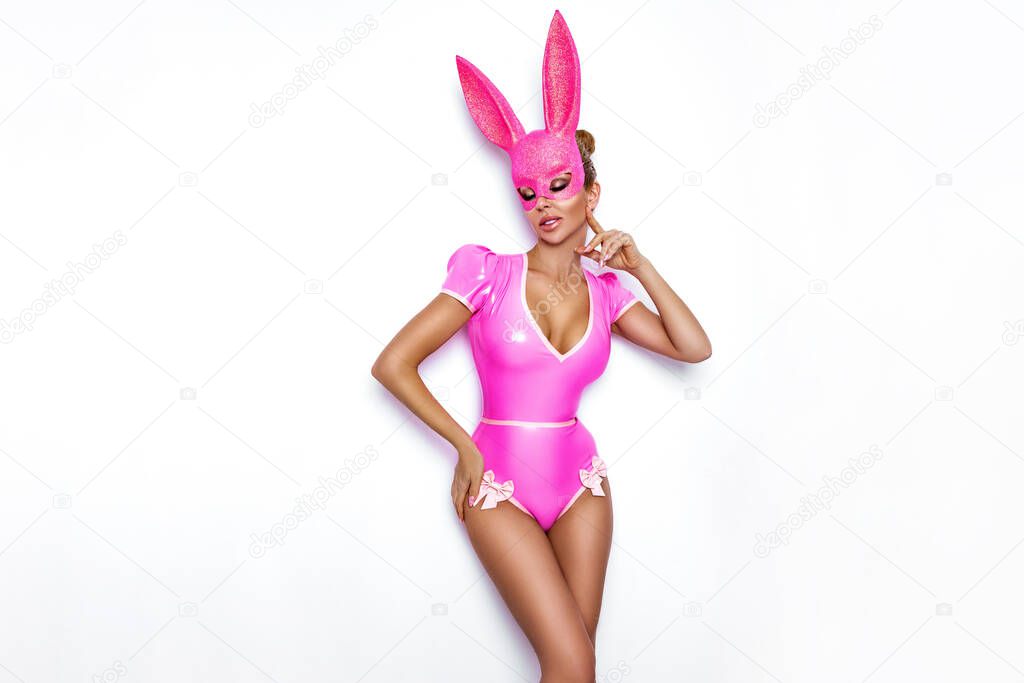 Sexy blonde woman posing in latex pink costume and pink bunny mask on white background. Easter bunny concept. Latex lingerie. Naughty girl. Halloween costume. Lingerie fashion.