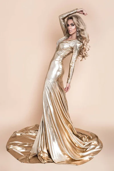 エレガントなファッション エレガントな長い金のドレスとベージュの背景に完璧な髪型で見事なブロンドの女性 豪華な夜のファッション グラマーファッションモデル 優雅さ 黄金のドレス — ストック写真