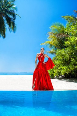 Lüks moda. Zarif bir manken. Maldivler plajında kırmızı uzun elbiseli şık bir kadın manken. Zarafet. Havuzun yanında kırmızı elbiseli klas bir kadın. Özel tasarım. Vogue.