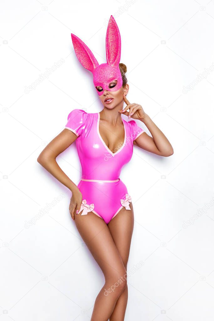 Sexy blonde woman posing in latex pink costume and pink bunny mask and pink balloons on white background. Easter bunny concept. Latex lingerie. Naughty girl. Halloween costume. Woman with balloons.