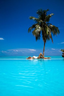 Tropikal Maldivler adasında havuzda beyaz mayo giymiş zarif bir kadın. Havuzdaki güzel bikinili kız, ufukta manzaralı. Güzel Hint okyanus manzarasında havuzun yanında zarif bir model. Seyahat