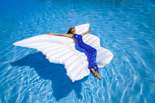 Uzun elbiseli şık manken havuzda bir şiltenin üzerinde yatıyor. Zarafet. Muhteşem elbiseli klas kadın Maldivler adasındaki havuzda poz veriyor. Özel tasarım. Vogue. Siren.